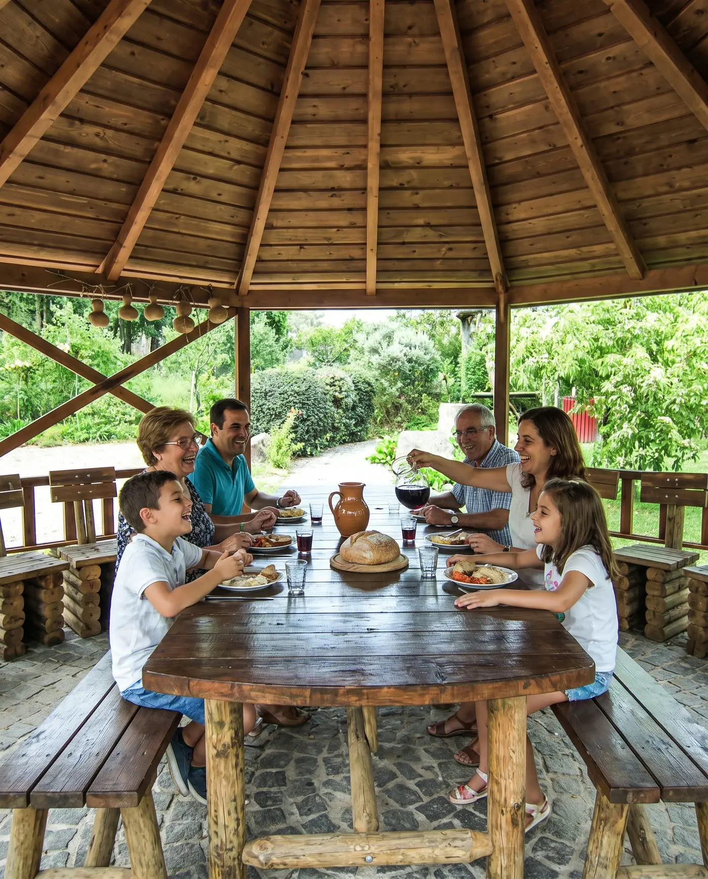 Een familie van drie generaties aan de lunch aan de lange tafel onder de houten veranda van de quinta